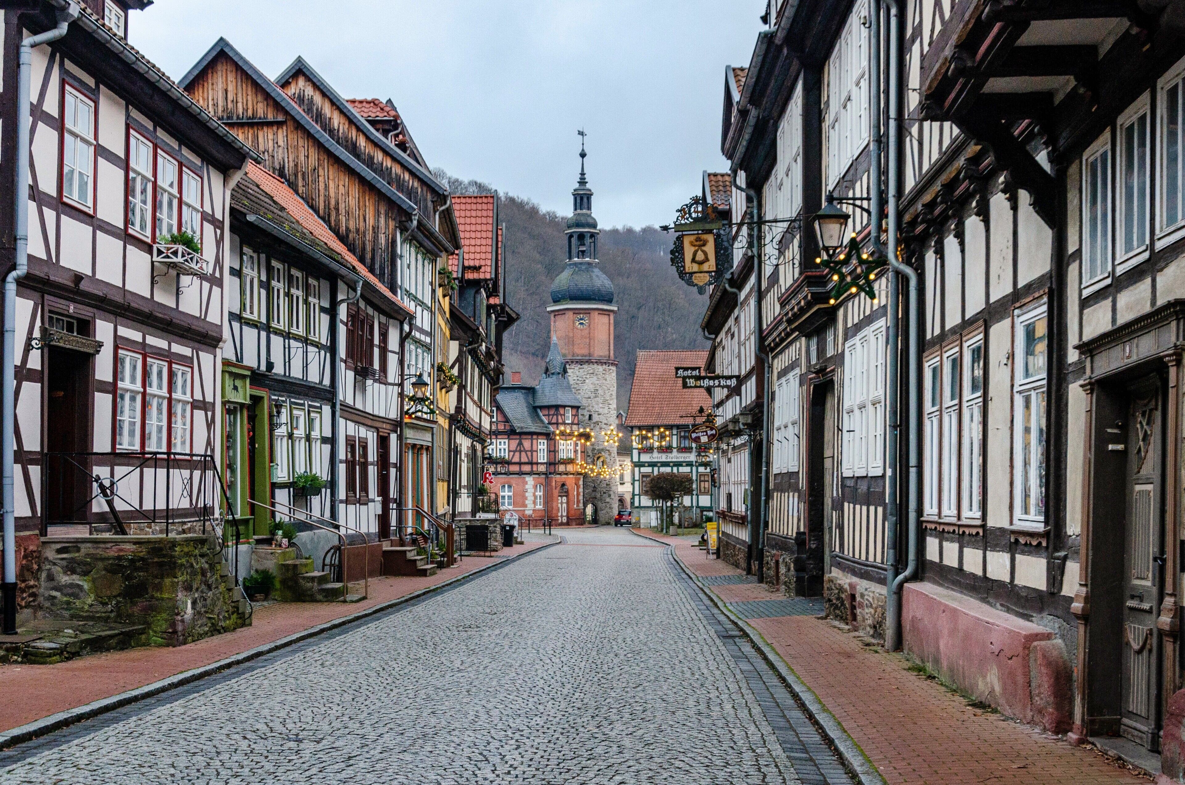 A cobblestone street lined with traditional half-timbered buildings, a church with a dome, and a hotel sign.
