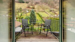 Ein Balkon mit zwei Stühlen und einem kleinen Tisch, mit Blick auf einen Garten mit Hecke und Bäumen.