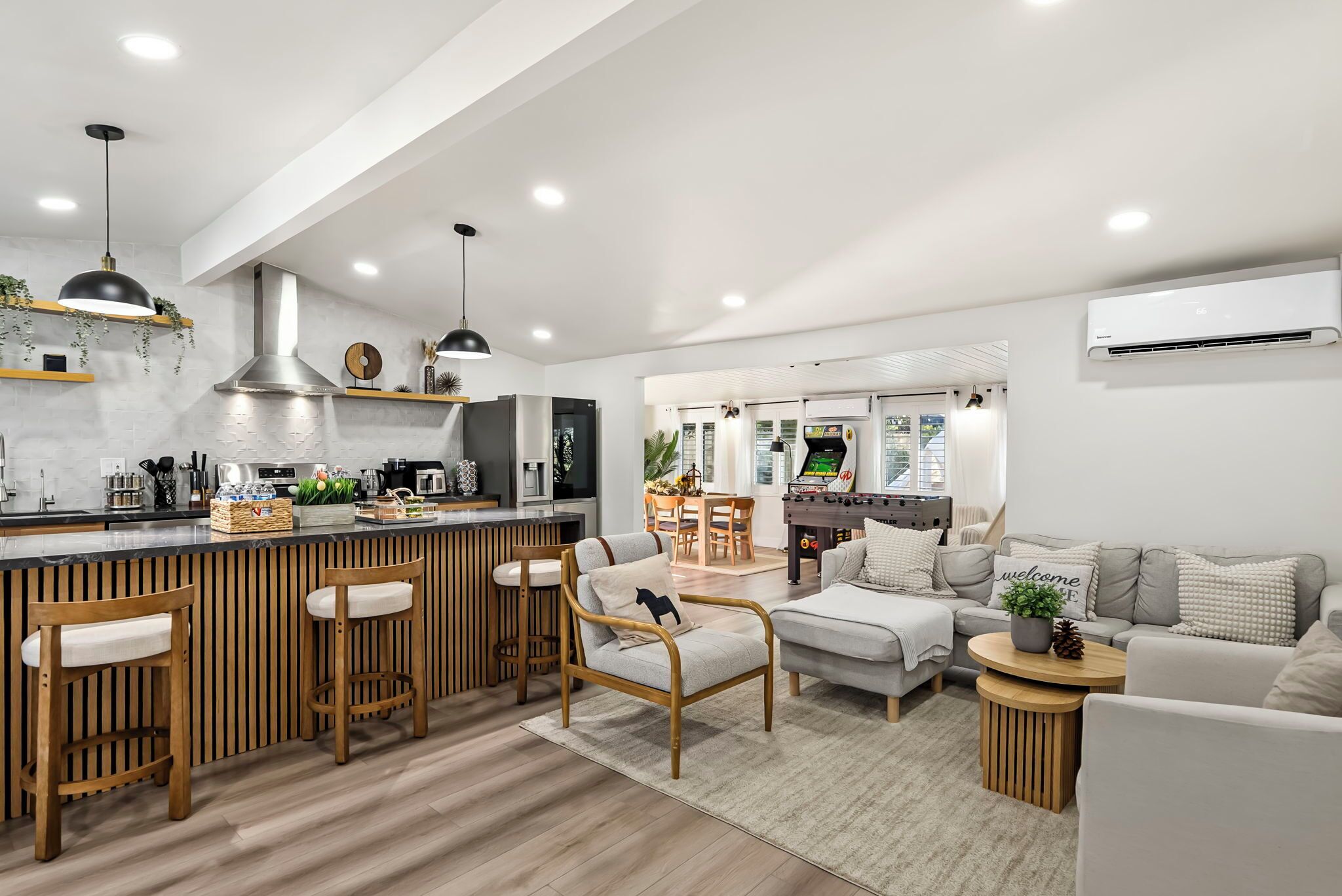 A modern kitchen with a bar area, wooden furniture, and a dining space with a foosball table.