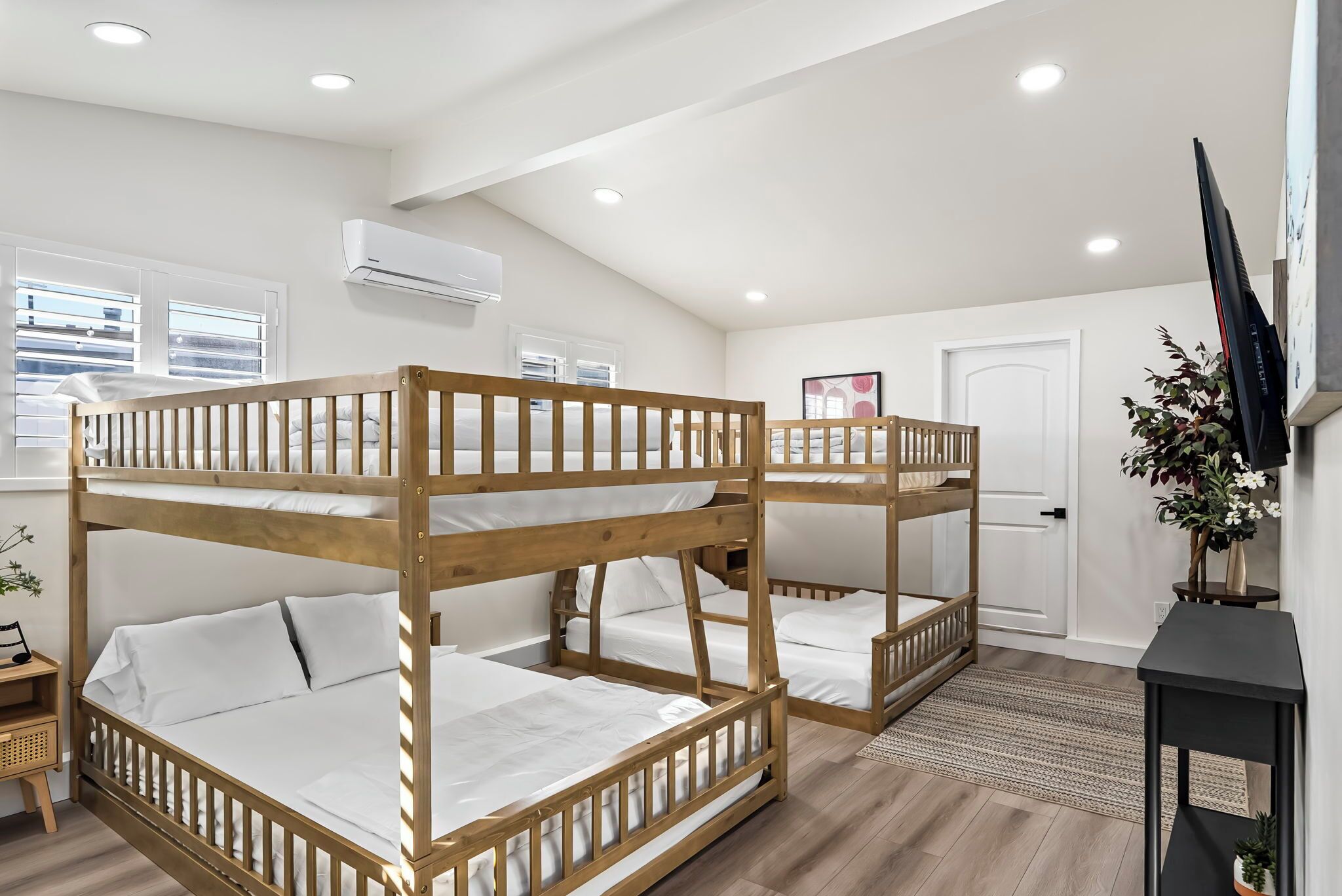 A room with bunk beds, a television, a door, and a window with blinds.