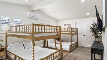 A room with bunk beds, a television, a door, and a window with blinds.