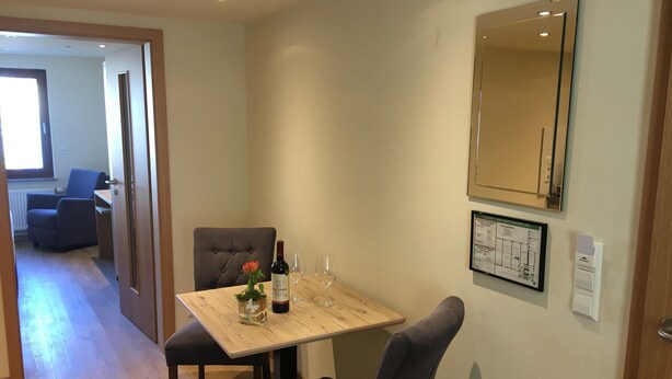 Un coin repas avec une table, des chaises, une bouteille de vin et des verres.