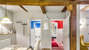 A modern interior with exposed wooden beams, a dining area with a table and chairs, a hallway leading to a bathroom, and a yellow armchair. - Apartment 'Ground Floor' (Stolberg i. Harz)