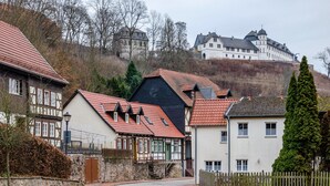 A traditional European town with historic buildings, including a prominent castle on a hill, and a mix of residential and commercial structures. - Apartment 'Ground Floor' (Stolberg i. Harz)
