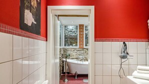 A bathroom with a red wall, a white bathtub, a towel rack, and a mirror. - Apartment 'Ground Floor' (Stolberg i. Harz)