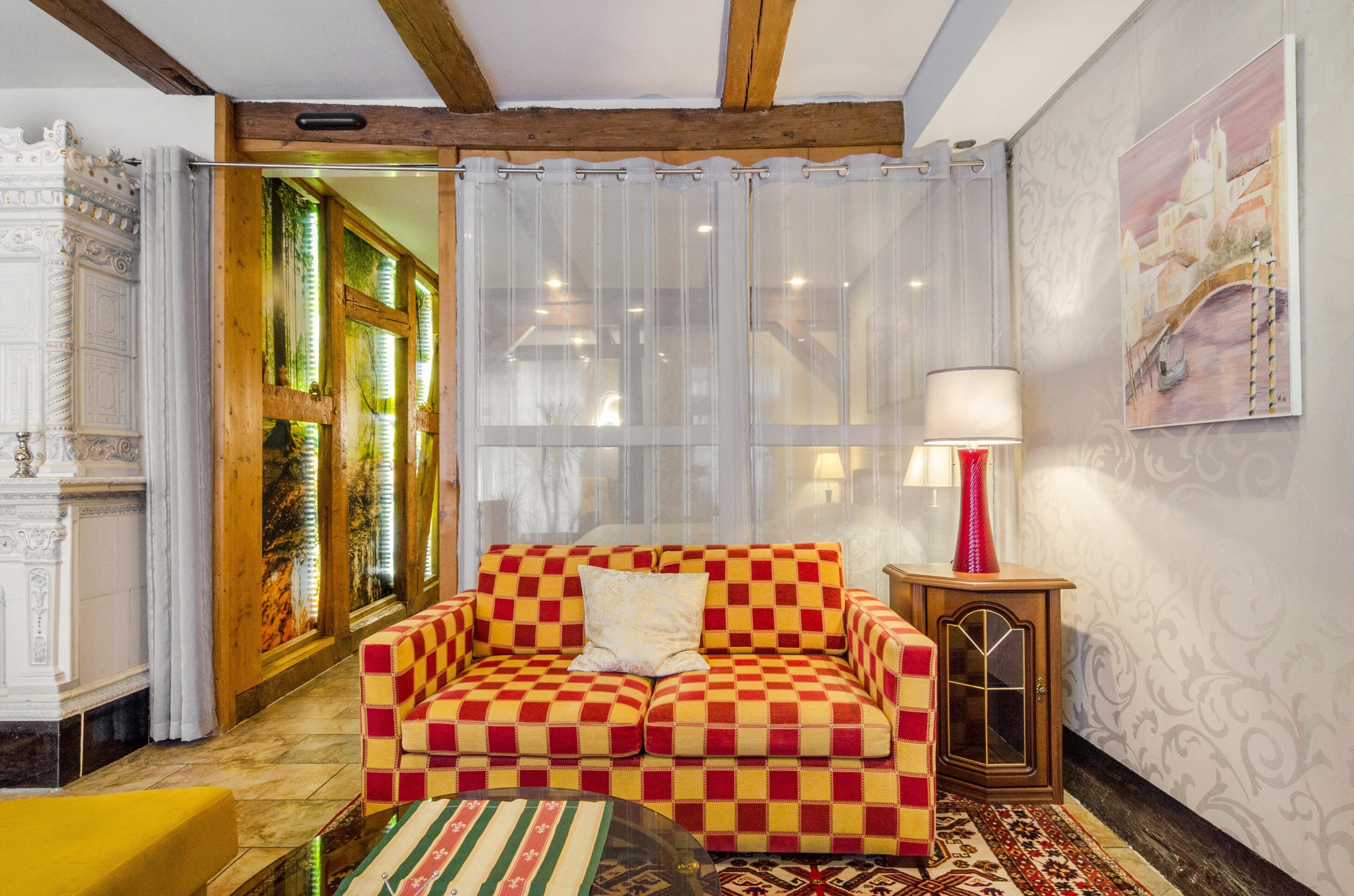 Um sofá xadrez, uma luminária e um tapete estampado numa sala com teto de madeira e um quadro na parede.