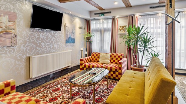 A hotel lobby with a checkered sofa, a yellow armchair, a patterned rug, a television, and a large window with curtains. - Apartment 'Ground Floor' (Stolberg i. Harz)