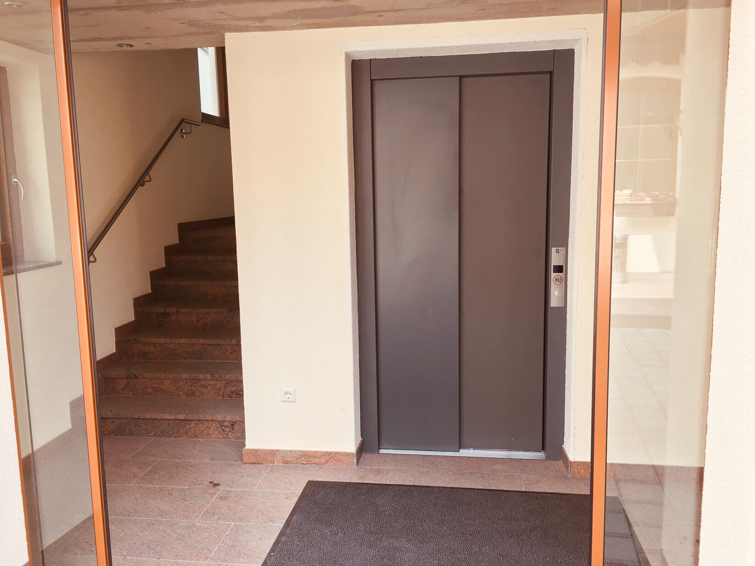 A staircase leading to a dark-colored door with a security lock, a glass door frame, and a doormat on the floor.