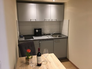 A compact kitchen with grey cabinets, a built-in dishwasher, a coffee machine, and a dining table with a wine bottle and glasses. - Apartment '3' with Shared Terrace and Wi-Fi (Mössingen)