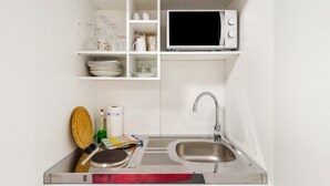 A compact kitchen with a microwave, sink, and shelves containing dishes and glassware. - Apartment "Double Room with Private Bathroom" (Stolberg i. Harz)