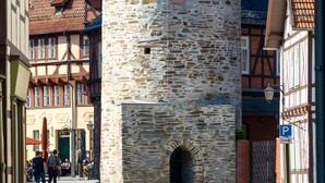 A stone tower with a small window, surrounded by traditional buildings with tiled roofs. - Apartment "Double Room with Private Bathroom" (Stolberg i. Harz)