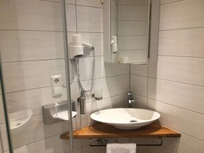 Ein Badezimmer mit einer Duschkabine, einem weißen Waschbecken und einem Holzlagerfläschchen.