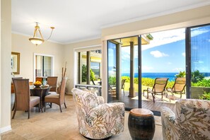 A spacious room with a dining area, a sofa, and a view of the ocean through large sliding doors.