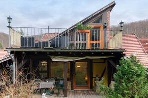 A two-story house with a balcony, a wooden deck, and a covered outdoor seating area.