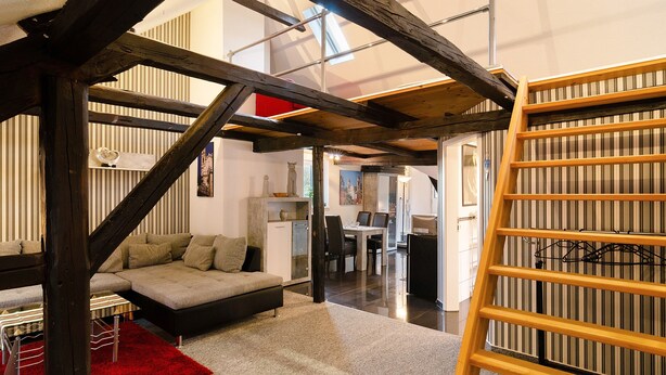Un interior moderno con vigas de madera a la vista, un sofá, un comedor y una escalera.