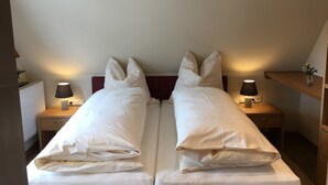 Une chambre double avec deux lits, des lampes de chevet, une tête de lit en bois et une petite étagère avec une plante.