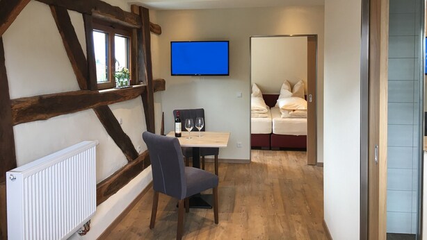 Une pièce avec un plafond en bois, un radiateur blanc, une table avec deux chaises, un téléviseur fixé au mur et un lit avec une literie rouge.