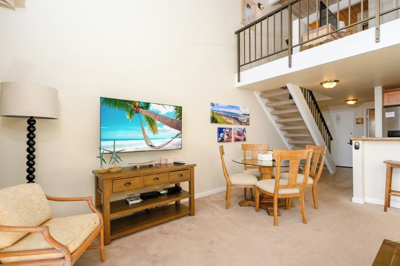 A living room with a TV, wooden furniture, a dining table, and a staircase leading to an upper level.