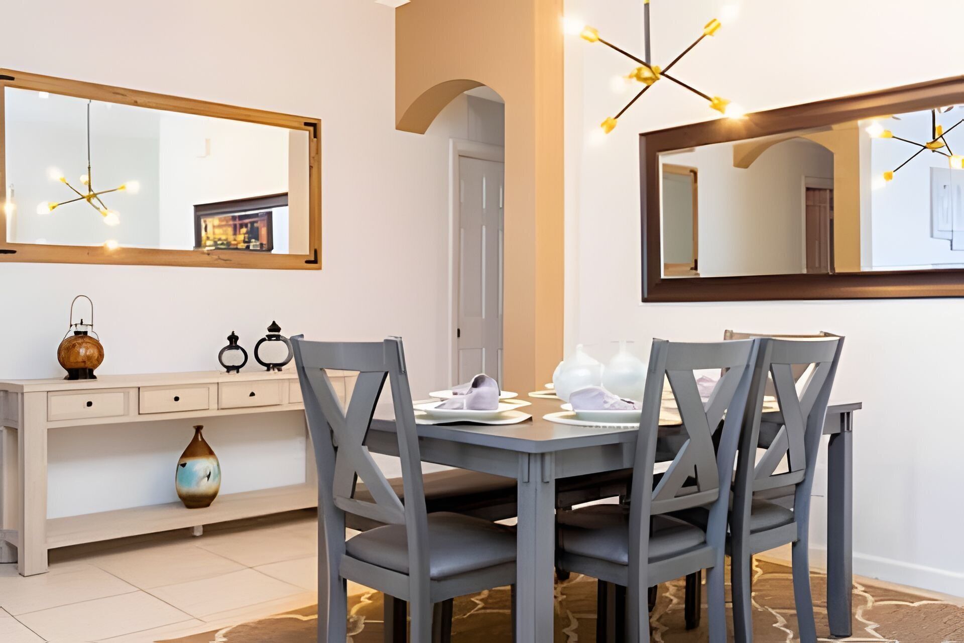 Un comedor con una mesa consola blanca, sillas grises y una araña.