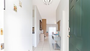 Ein moderner Flur mit einer grünen Tür, weißen Wänden und einem gefliesten Boden. An der Wand hängen gerahmte Bilder und eine Deckenleuchte.