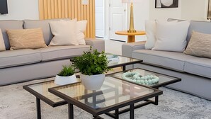 Una sala de estar moderna con dos sofás grises, una mesa de centro de vidrio y una mesita de noche con una lámpara.