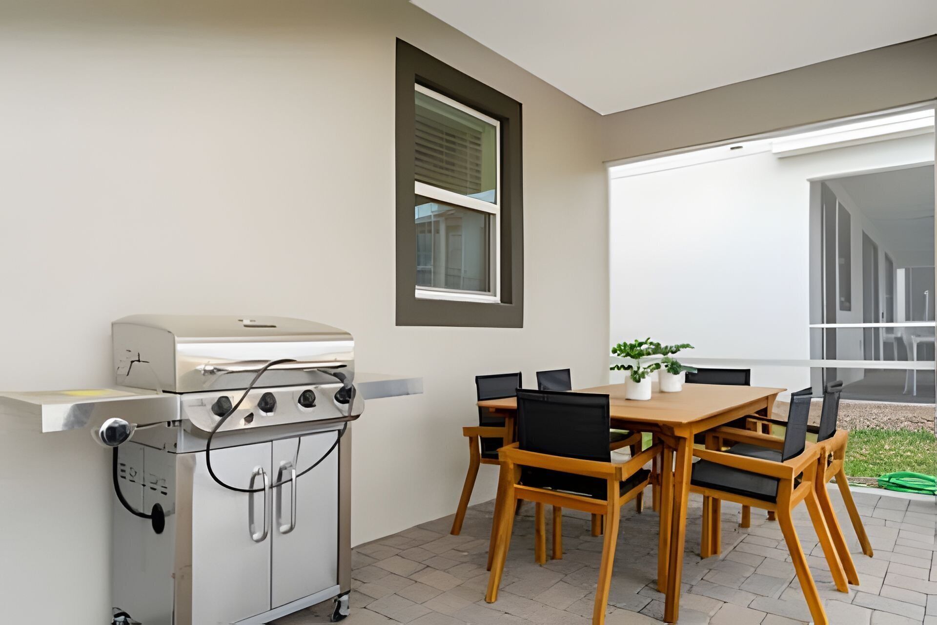 Une terrasse avec un barbecue, une table avec des chaises et une fenêtre avec des stores.