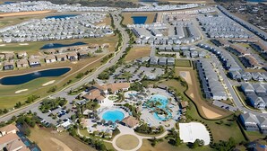 Vista aérea de un resort con múltiples piscinas, un campo de golf y un amplio estacionamiento.