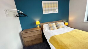 Una cama bien tendida con un edredón amarillo, dos lámparas de noche y una mesita de noche de madera con cajones.