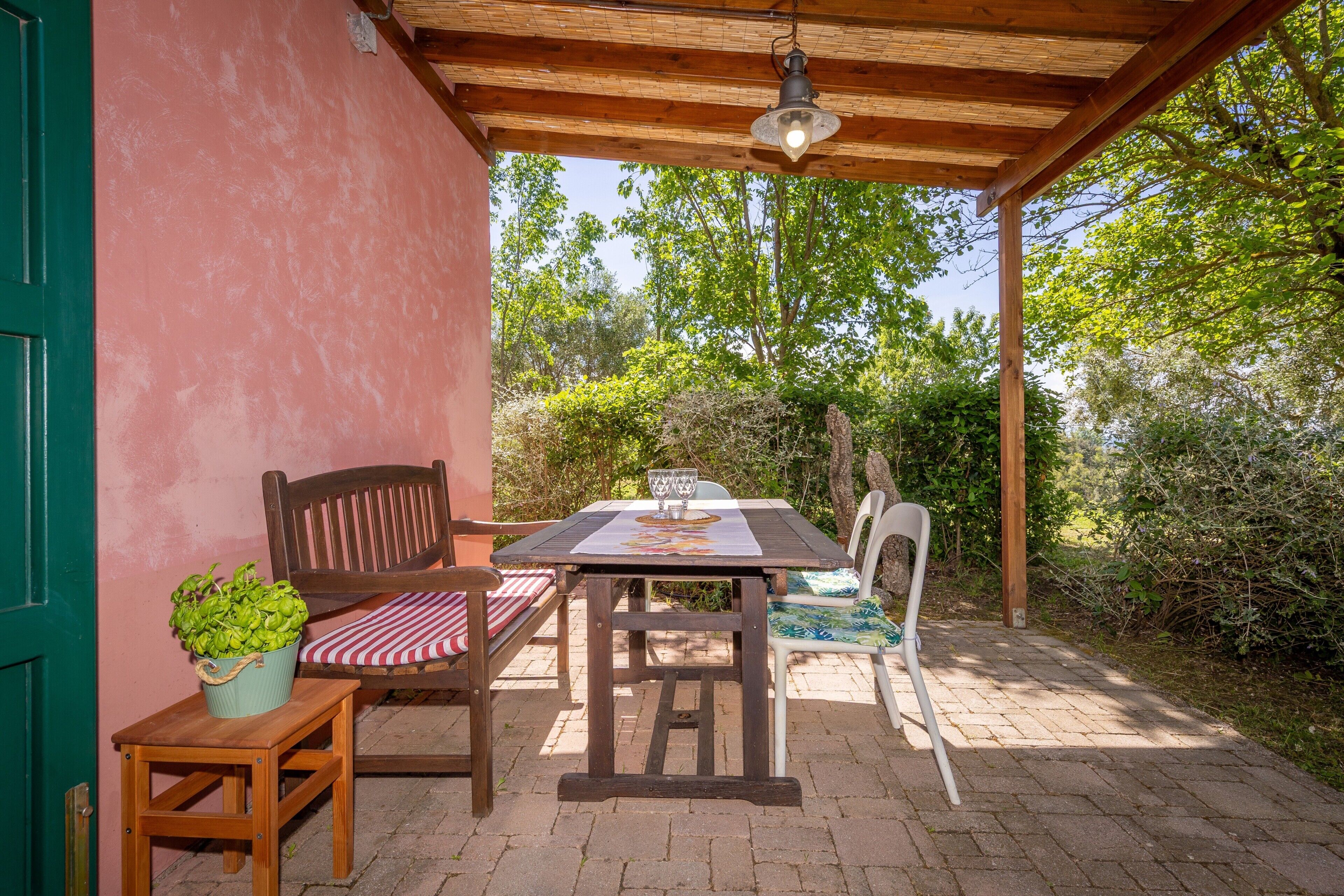 An outdoor patio with a wooden table, two chairs, a bench, and a potted plant.