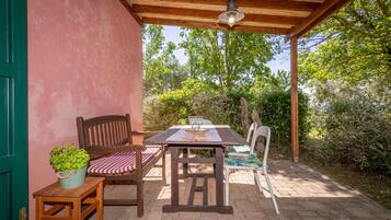 An outdoor patio with a wooden table, two chairs, a bench, and a potted plant.