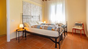 A bedroom with a bed, bedside lamps, a chair, a window with curtains, and a wall-mounted air conditioner.