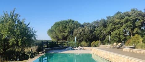 A swimming pool with lounge chairs, surrounded by trees and a stone deck.