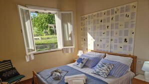 Un dormitorio con una cama, un banco, un ventanal y una pared con un tablón de anuncios.