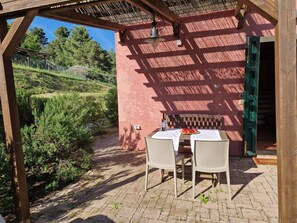An outdoor patio with a table and chairs, a pergola, and a view of a hillside.