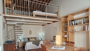 Een slaapkamer met een vide, voorzien van een stapelbed, een eethoek met houten stoelen, een spiltrap en een boekenkast.