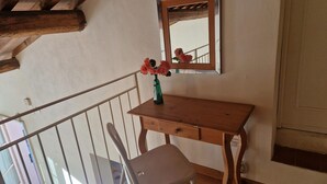 Een kamer met een houten bureau, een stoel, een spiegel en een vaas met bloemen.