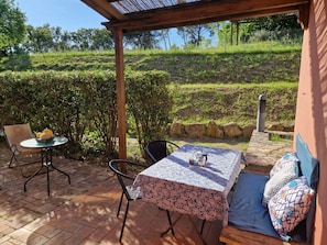 Une terrasse extérieure avec une table et des chaises, un espace salon couvert et une vue sur un paysage verdoyant.