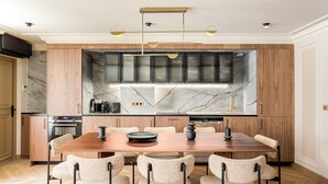 A modern kitchen with a marble backsplash, wooden cabinets, and a dining area with a wooden table and chairs. - Merveil Signature Suite - Bateliere (Paris)