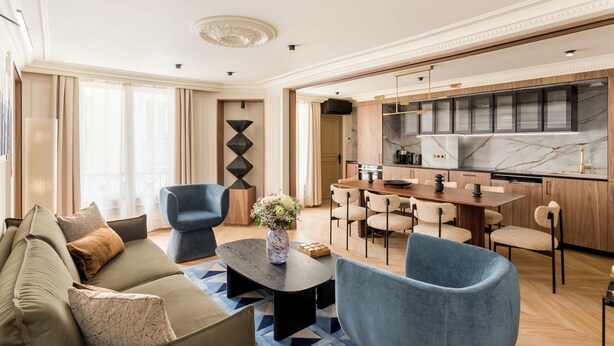 A modern living room with a sofa, chairs, a coffee table, and a kitchen area with a dining table and chairs. - Merveil Signature Suite - Bateliere (Paris)