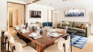 A spacious dining area with a long wooden table set for six, flanked by upholstered chairs. A television is mounted on the wall, and a sofa is positioned in the background. - Merveil Signature Suite - Bateliere (Paris)