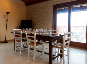 A dining area with a stone wall, a balcony with white chairs, and a television. - Cottage 'Gîte Télégraphe, Sonnay' with Mountain View, Shared Pool and Wi-Fi (Sonnay)