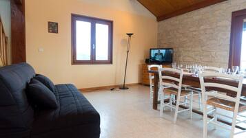 A living room with a sofa, a dining area with a table and chairs, a television, and a stone wall.