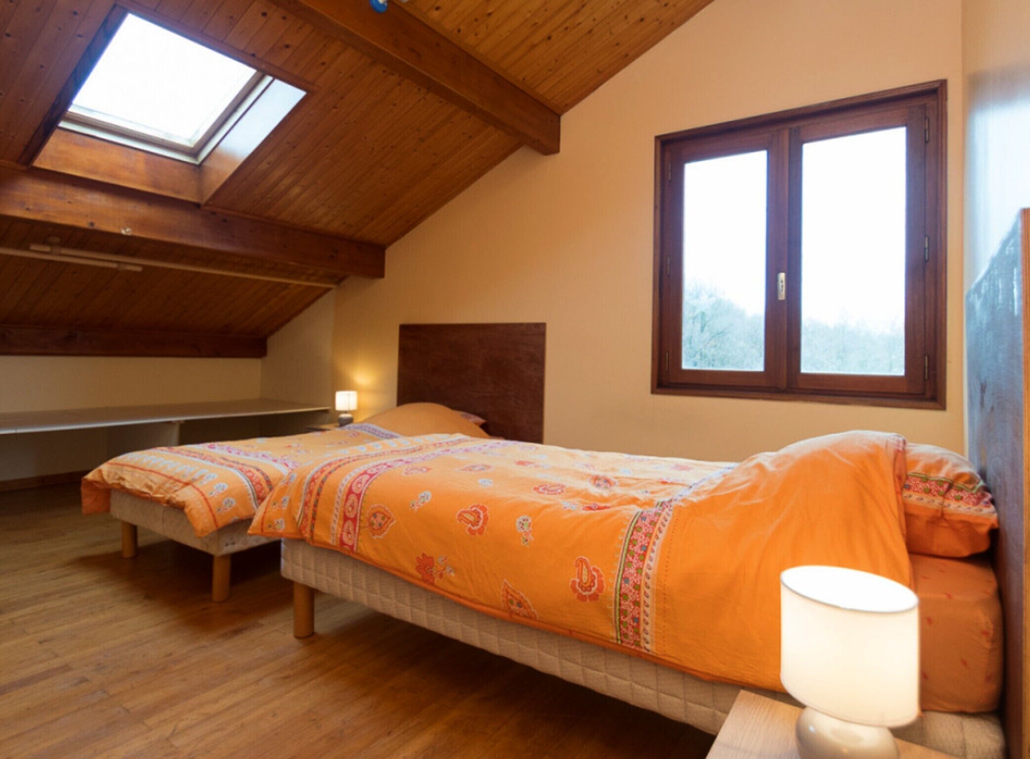 A room with two beds, a skylight, a window, and a lamp.