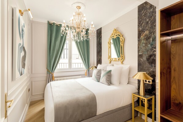 A bedroom with a large bed, a chandelier, a mirror, and a nightstand. - Merveil Signature Suite - Hoche (Paris)