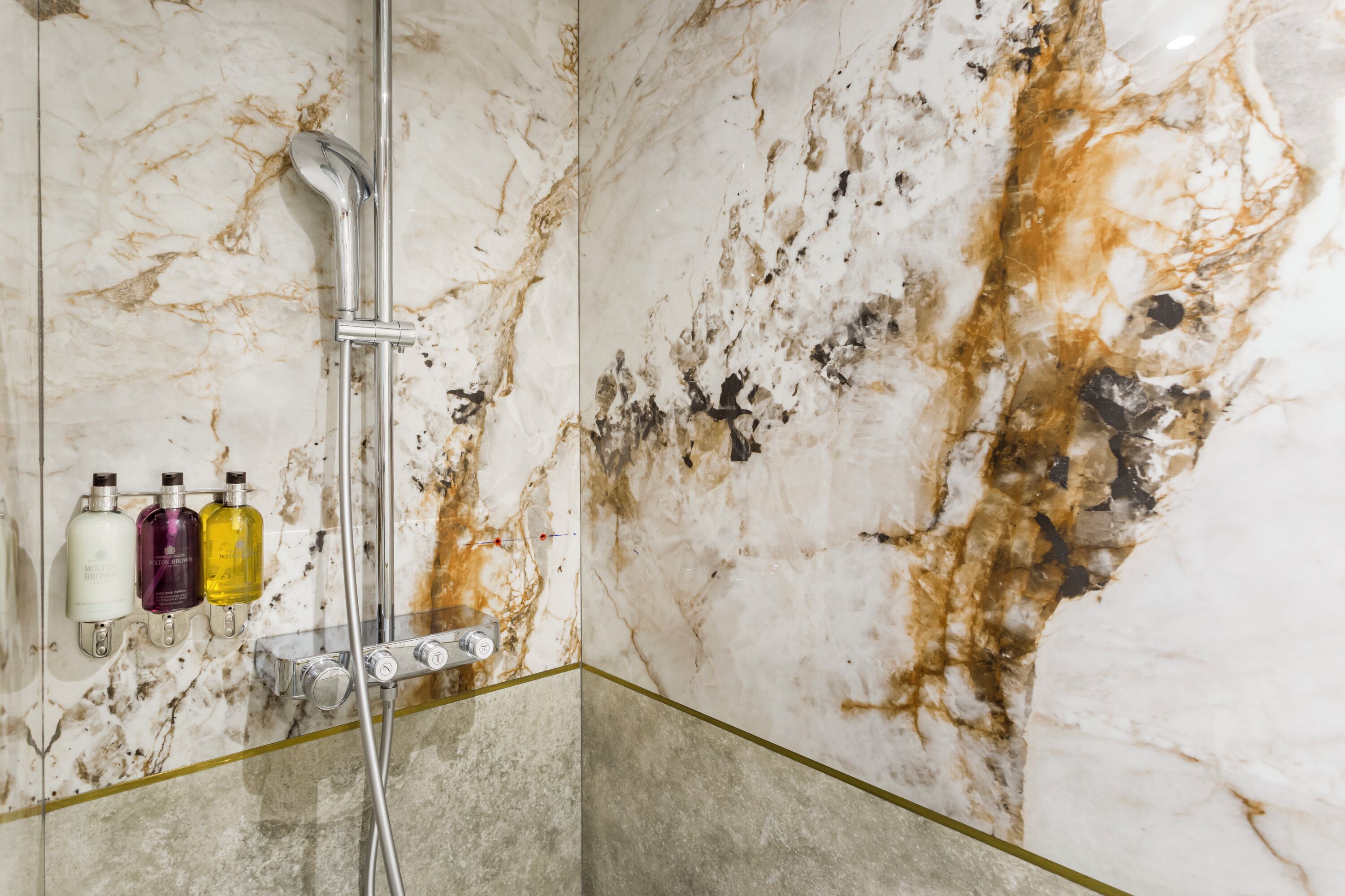 Ein Badezimmer mit Marmorwand, einer Duschkabine aus Glas und drei Toilettenartikeln.