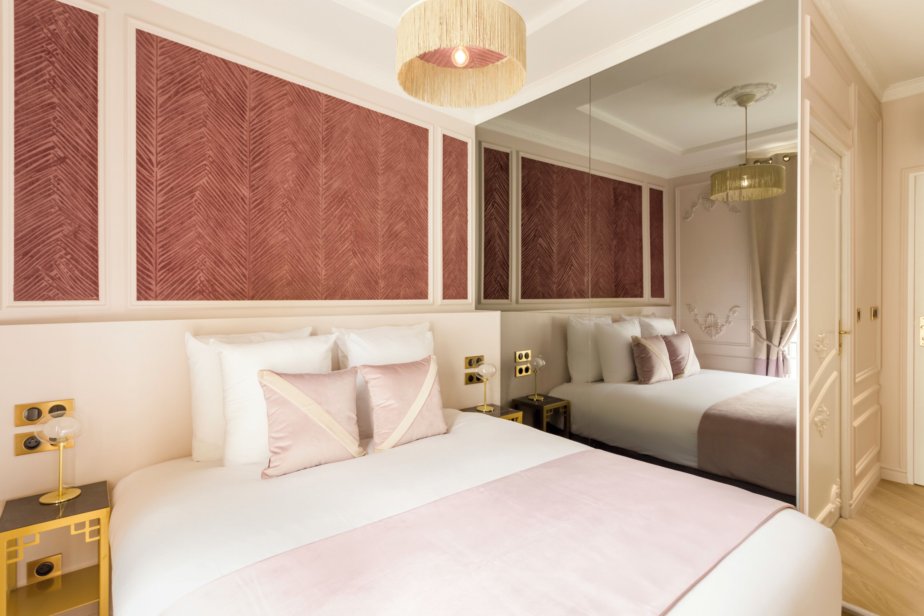 Habitación de hotel moderna con una cama grande, una mesita de noche con lámpara y un espejo sobre la cama.