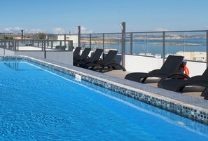 A rooftop pool with clear blue water, surrounded by lounge chairs and a glass balustrade offering a view of the sea. - Cora Sun Hotel  (St. Paul's Bay)