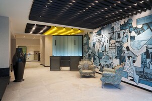 Een moderne lobby met een grote muurschildering, een receptiebalie en een bijzondere fauteuil met een patroon.