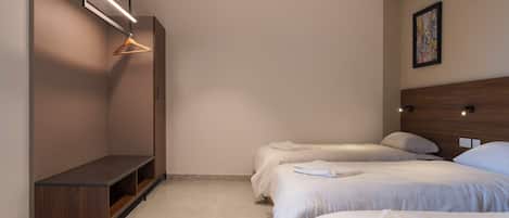 A modern hotel room with two beds, a wooden bench, a hanging light, and a painting on the wall.