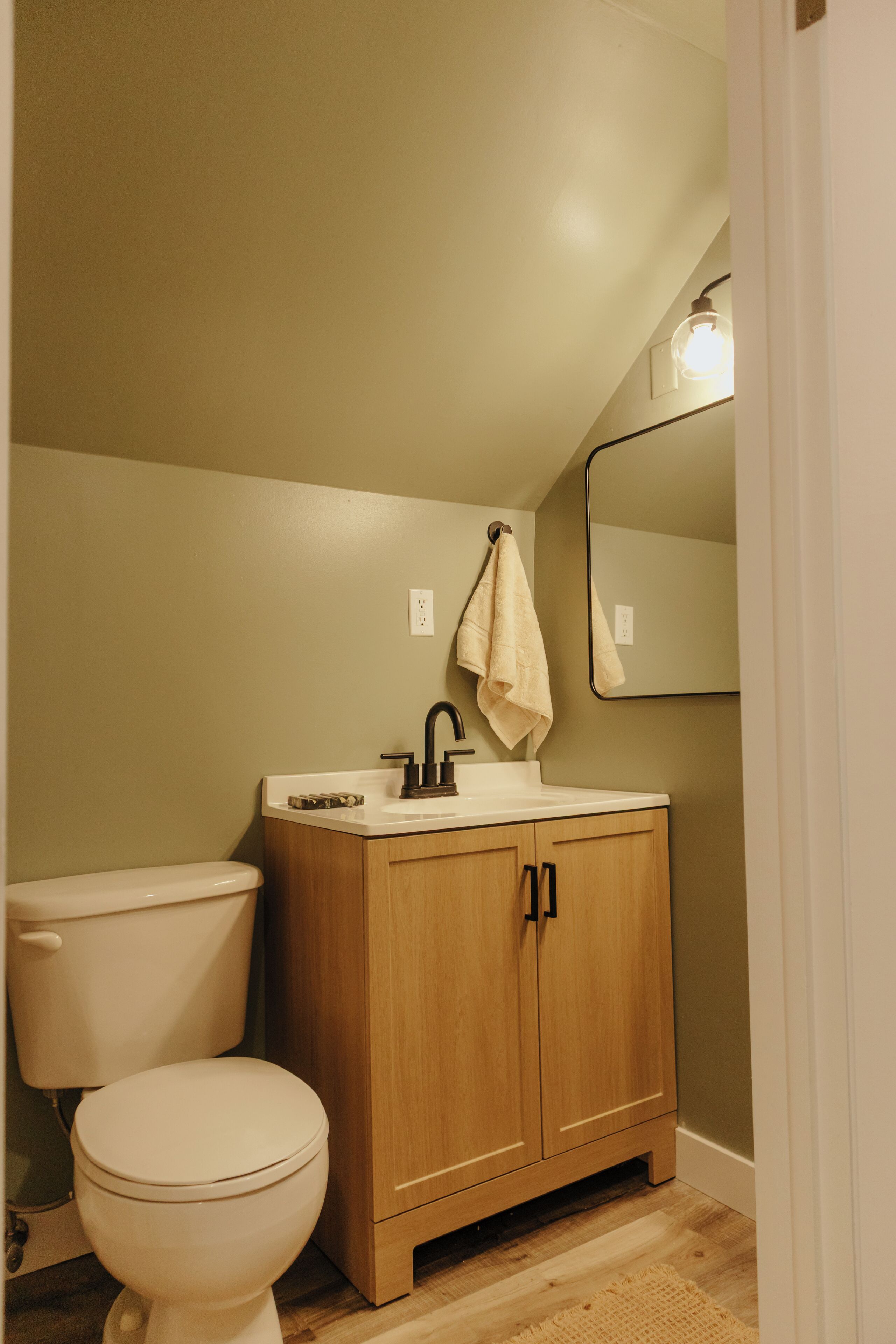 A bathroom with a toilet, sink, wooden cabinet, and a mirror.